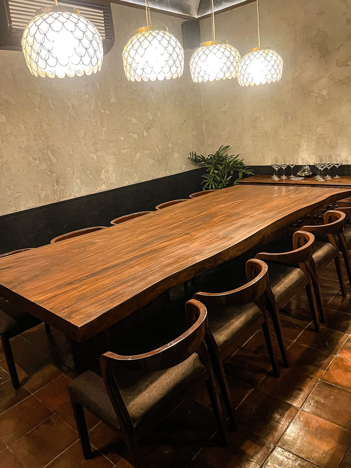 Four capiz shell scallop pendant lights above a live-edge solid wood private dining table at Toma Toma, Makati