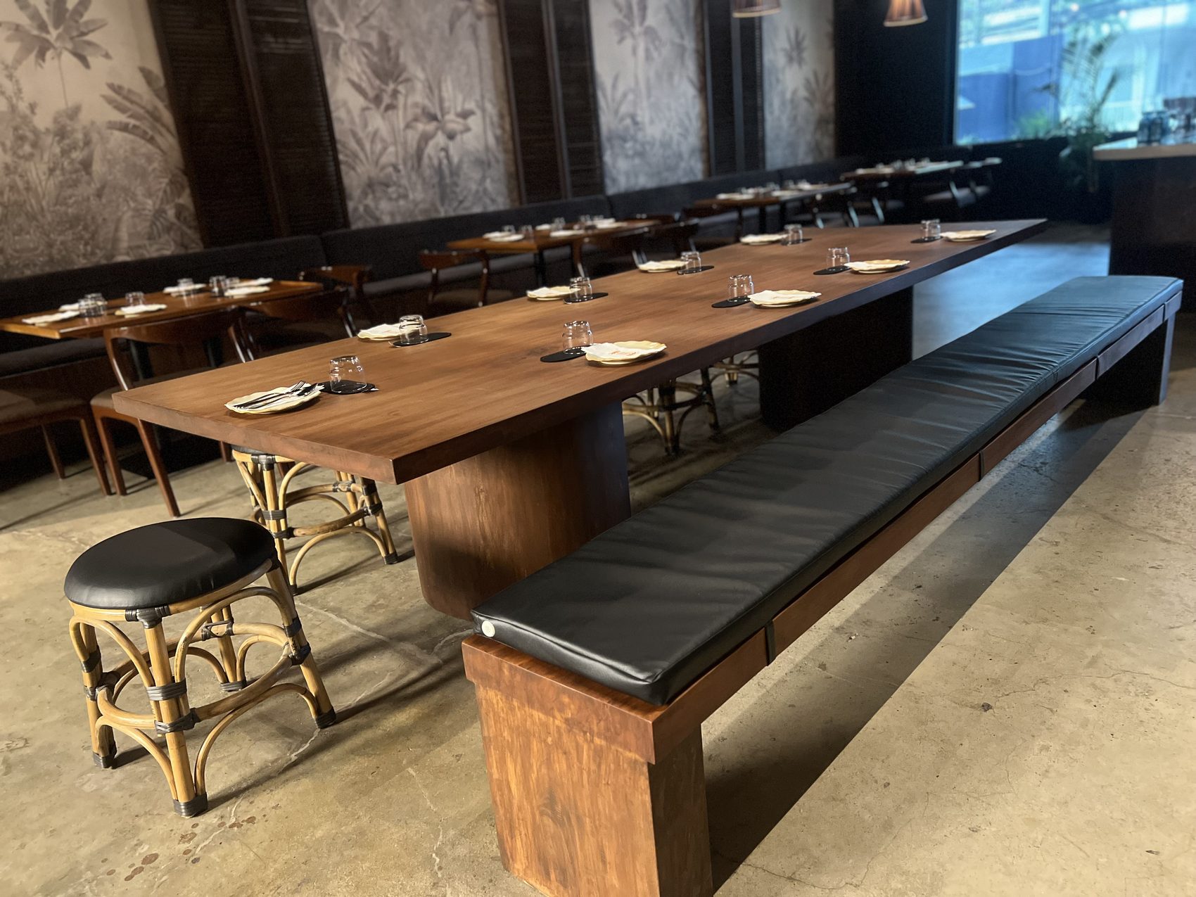 Long live-edge communal dining table with a matching solid wood bench and a rattan stool at Toma Toma, Makati